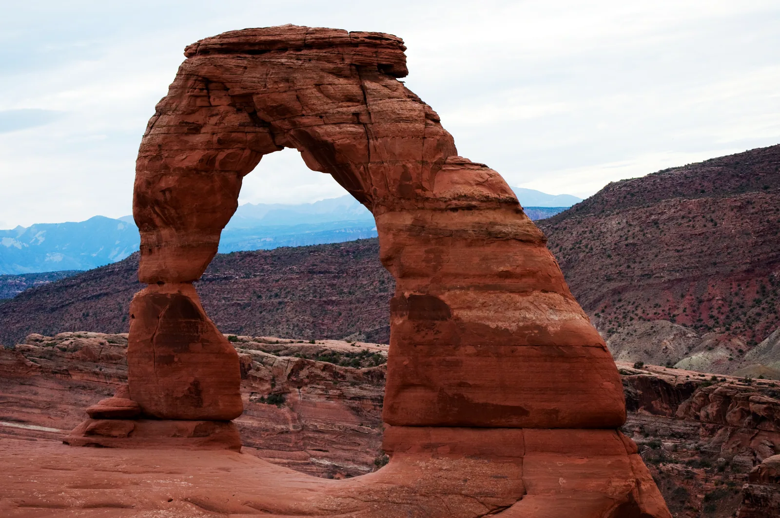 Delicate Arch standing alone on its sandstone bowl with the La Sal Mountains behind.