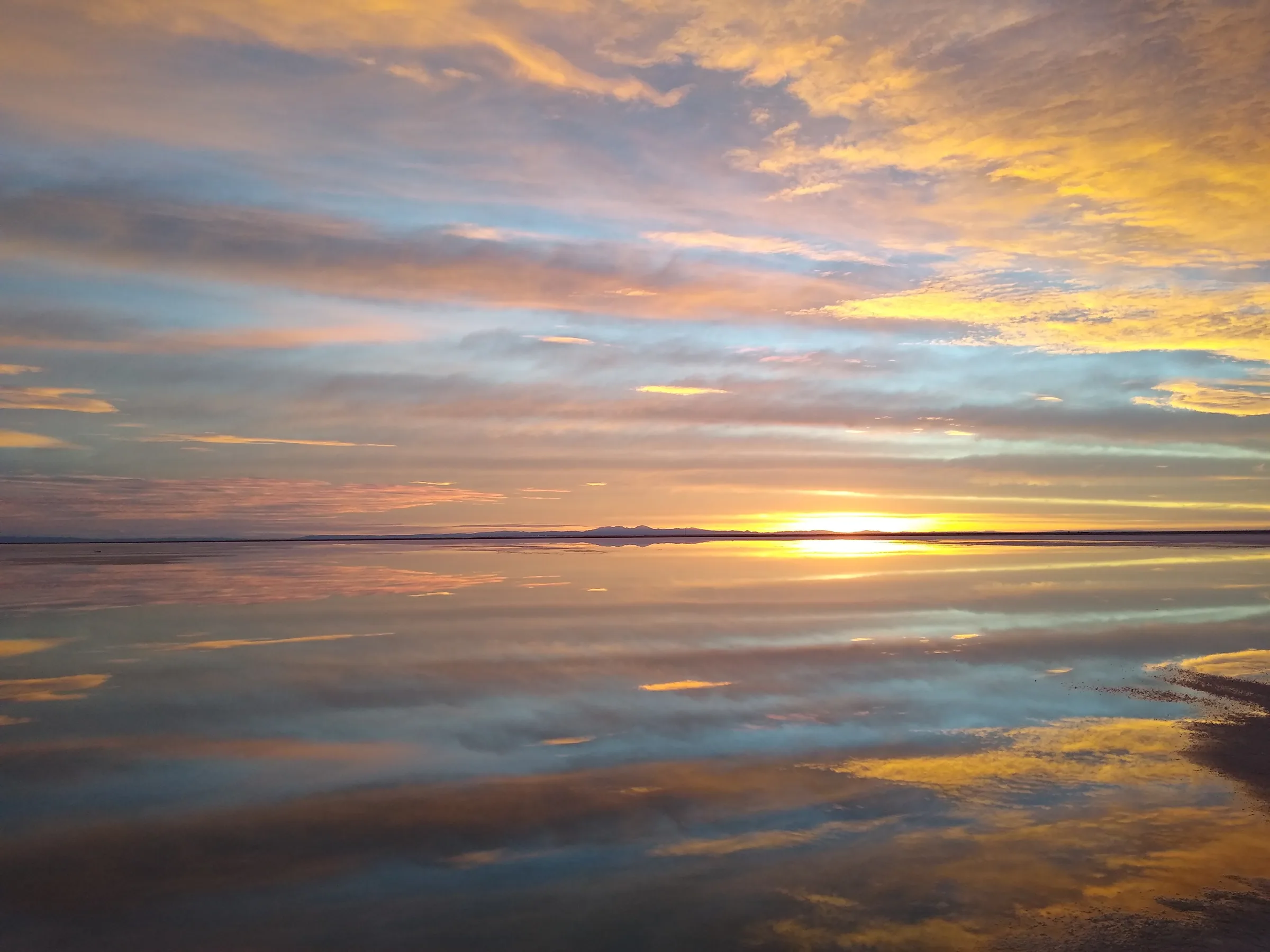 A shallow layer of water standing on the Bonneville Salt Flats at sunrise, reflecting the sky end to end