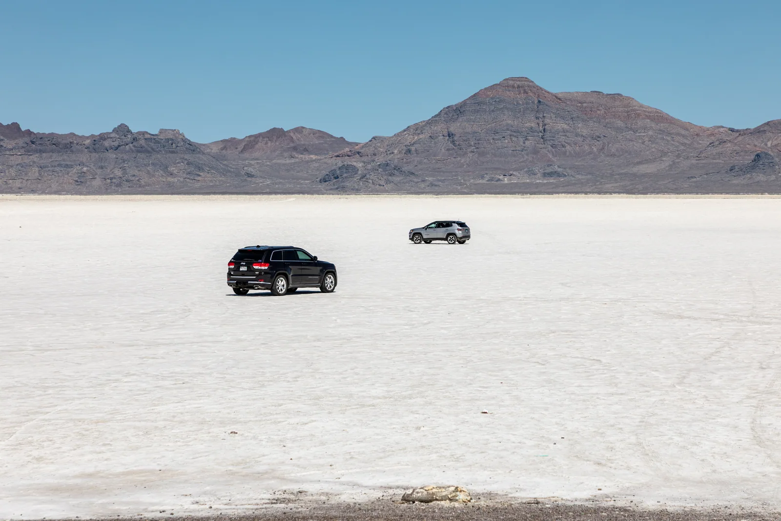 Two cars alone on the Bonneville Salt Flats, dwarfed by a white salt plain that runs to the mountains.